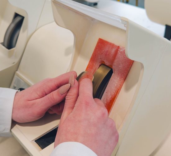 Étudiante en classe préparatoire d’optique-lunetterie en alternance utilisant une meule manuelle pour tailler un verre.