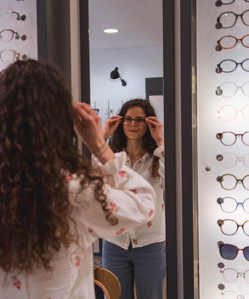Femme essayant une paire de lunettes de vue devant un miroir dans un magasin d'optique d'application.