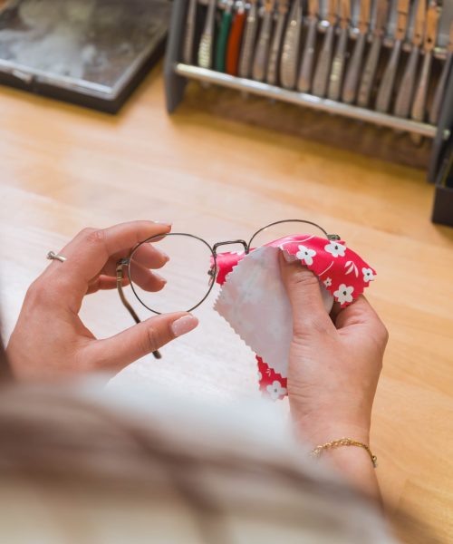 Étudiante opticienne nettoyant avec soin les verres d'une paire de lunettes rondes à l'aide d'une chamoisette.